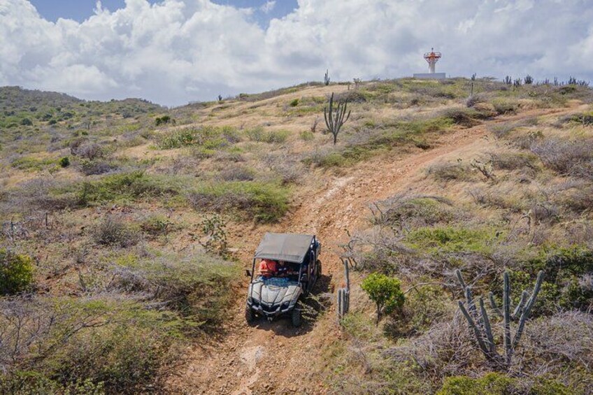 Un jeep en un camino de tierra en un paisaje desértico con vegetación escasa y un faro distante. 4