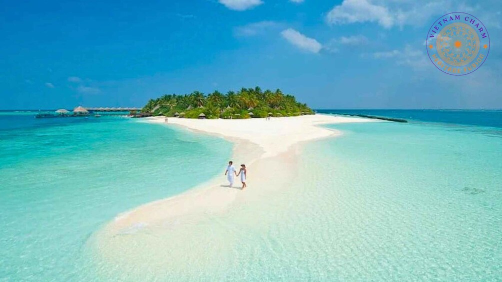 A couple walking on a white sandy beach with clear turquoise water and a small island with trees in the background. 1