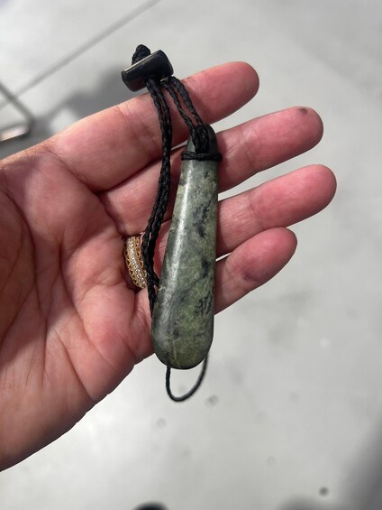 A hand holding a green stone pendant with a black cord. 4