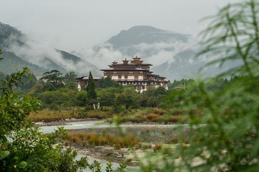 A traditional multi-tiered building surrounded by lush greenery and a river, with mountains in the background. 5
