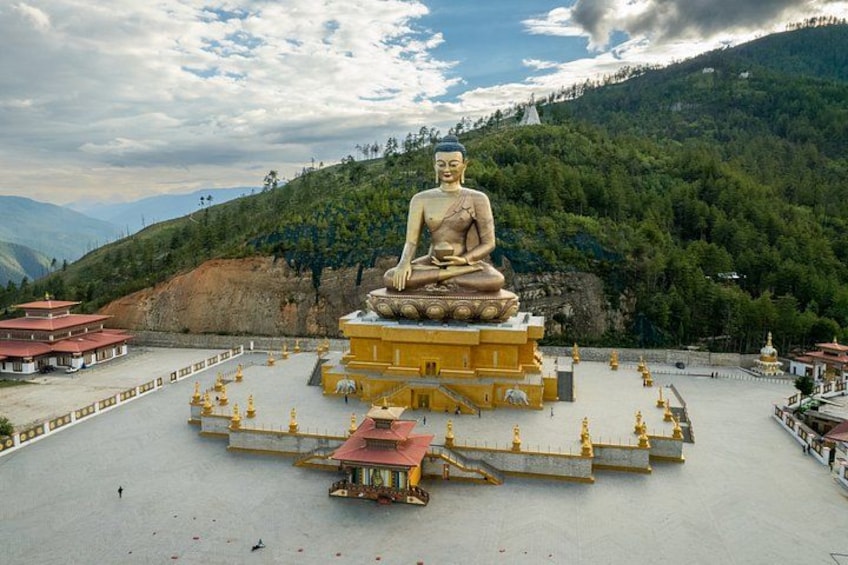 A large seated Buddha statue surrounded by a temple complex with a mountainous backdrop. 3