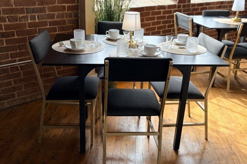 Une table à manger dressée avec des tasses et des soucoupes blanches, ainsi qu’un service à thé, entourée de chaises noires. 1