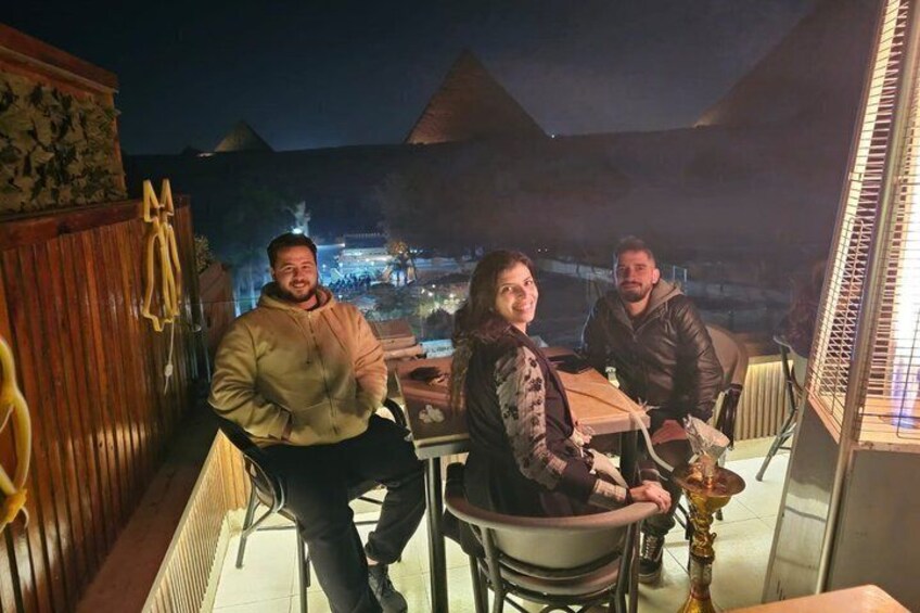 Tres personas cenando en una mesa con vistas a las pirámides de noche. 3