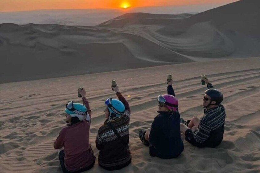 Vier Personen sitzen auf Dünen bei Sonnenuntergang. 3