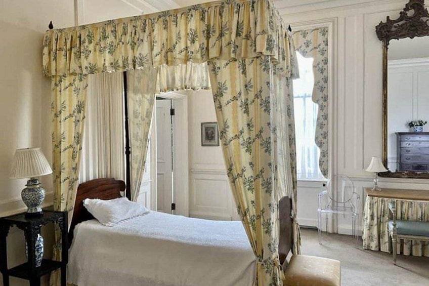 A four-poster bed with floral curtains, a bedside table with a lamp, and a dresser with a mirror. 3