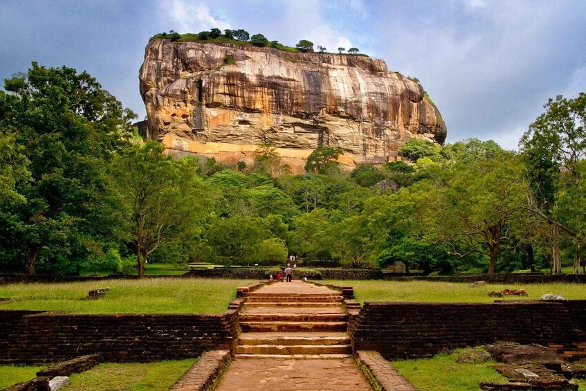 A large rock formation with a staircase leading up to it, surrounded by lush greenery. 1