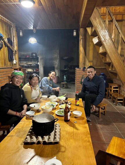 A group of people dining in a rustic wooden room with a brick stove in the background. 3