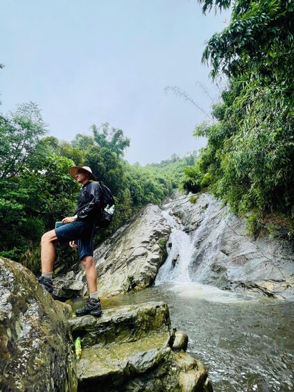 A person sitting on a rock by a waterfall in a forested area. 2