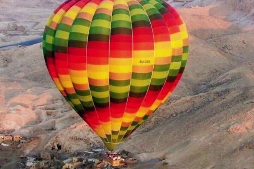 A colorful hot air balloon with the registration SU-240 flying over a desert landscape. 2