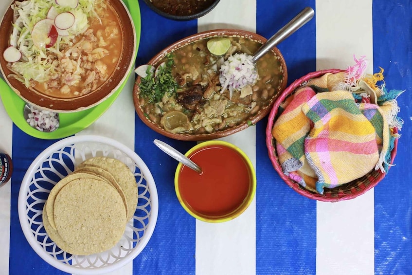 A table with various dishes, including a bowl of soup, a plate of tortillas, and a basket of colorful blankets. 5