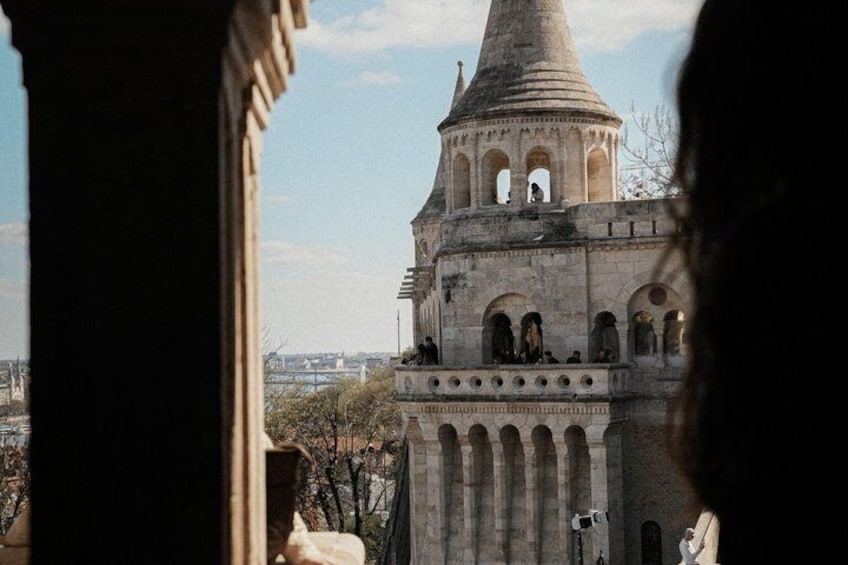 A historic tower with arched windows and a conical roof, viewed from behind a column. 1