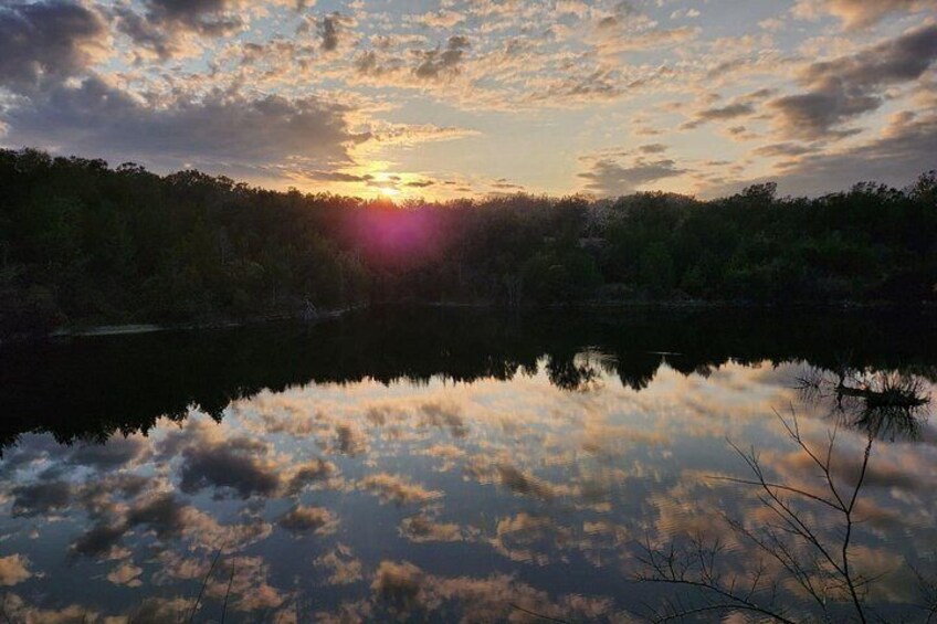 A sunset over a calm lake with reflections of the sky, surrounded by dense forest. 5