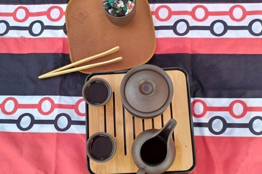 A traditional tea set with a teapot, cups, and chopsticks on a patterned cloth. 1