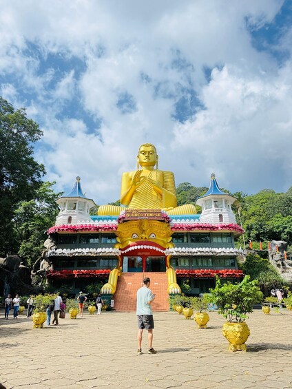 A large golden Buddha statue in front of a temple with a blue roof and a white tower. 1