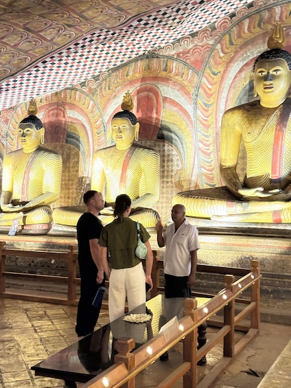 A group of people observing large golden Buddha statues with intricate designs on the ceiling. 4