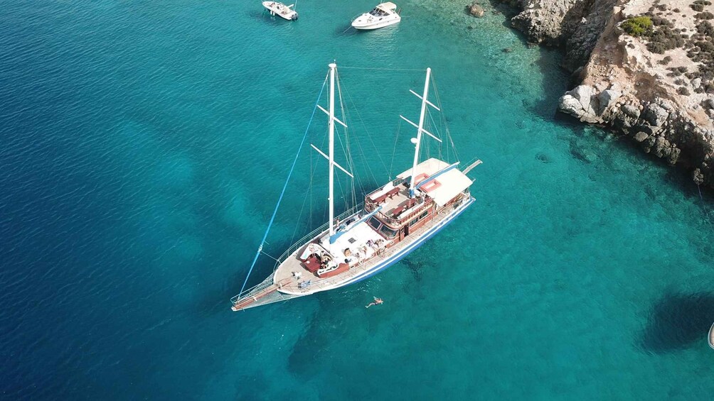 A sailboat anchored near a rocky coastline with clear turquoise water. 1