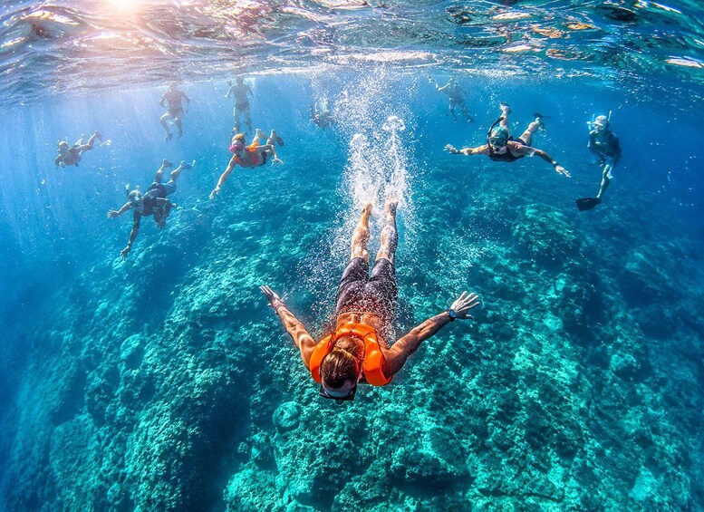 A person swimming underwater with others, surrounded by clear blue water and visible underwater rocks. 5