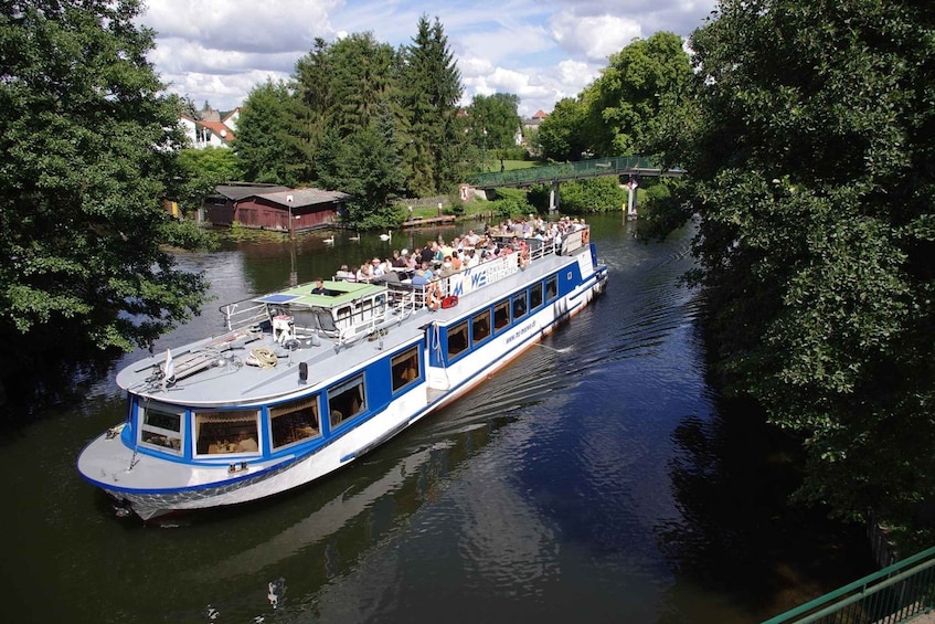 A riverboat with passengers, surrounded by trees and a bridge in the background. 2