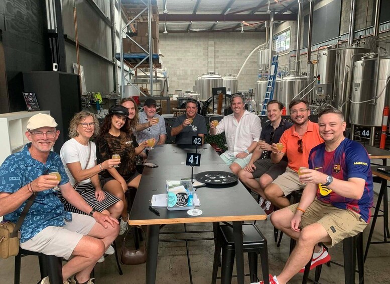 A group of people seated around a table in a brewery setting with stainless steel tanks and a sign reading 'Future 44'. 2