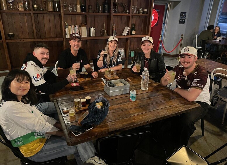 A group of people seated around a wooden table in a rustic setting with shelves in the background. 3