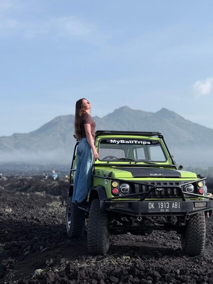 A green Suzuki vehicle with a license plate 'DK 1913 ABI' parked on rocky terrain with a person standing beside it. 2