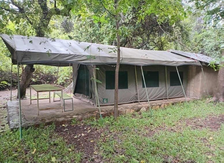A tent with a table set up in a forested area. 2