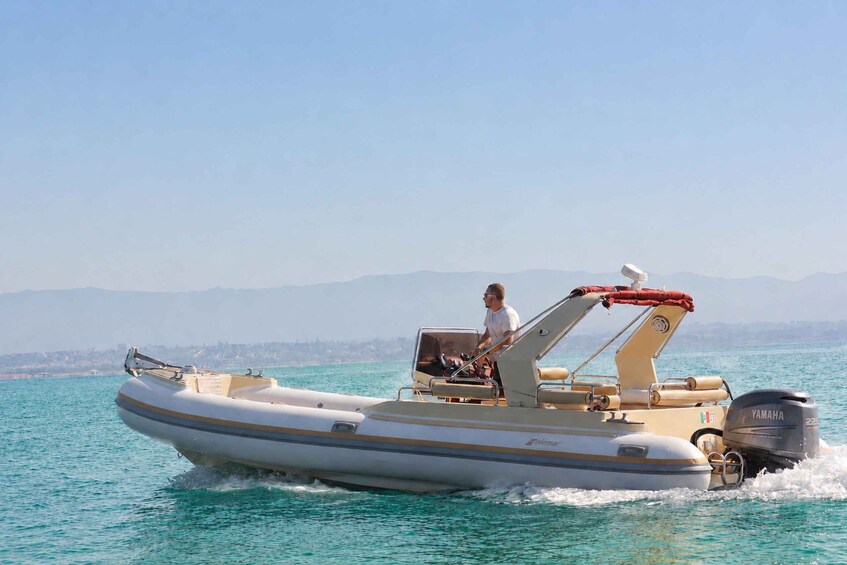 A small motorboat with a person on board, moving through turquoise water with a distant shoreline and mountains in the background. 4
