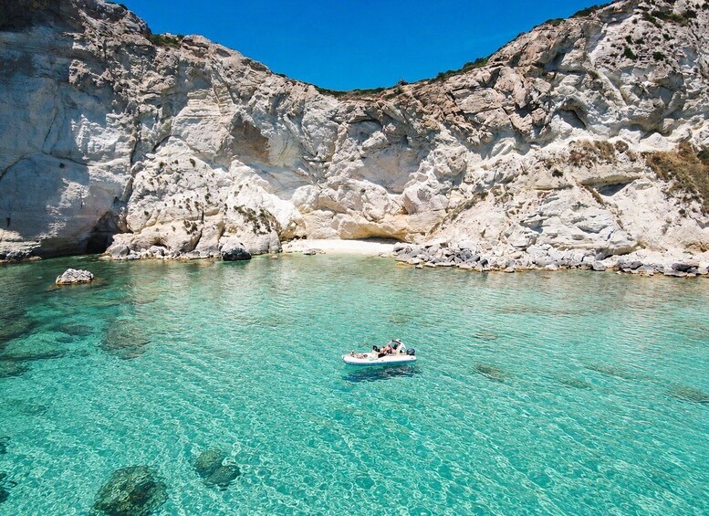 A clear turquoise sea with a rocky coastline and a person on a small inflatable boat. 1