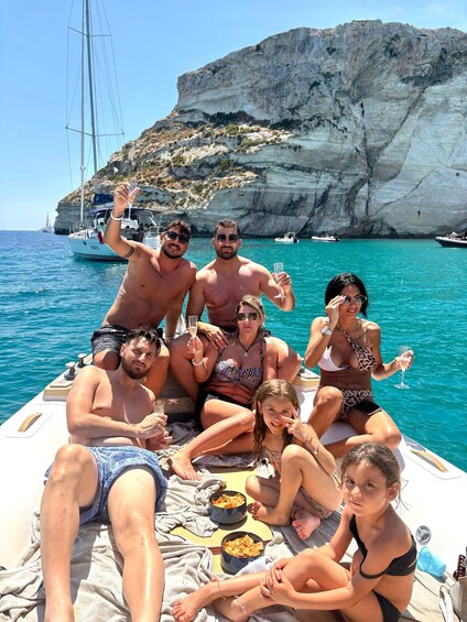A group of people on a boat with a rocky cliff and sailboats in the background. 5