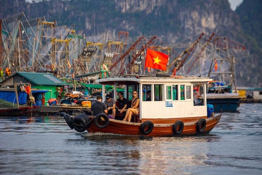 A boat with a Vietnamese flag, people on board, and a dock with fishing equipment in the background. 3