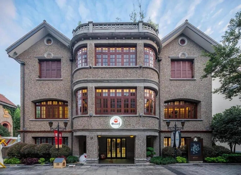 A two-story building with a stone facade, multiple windows, and a sign with a red emblem. 1