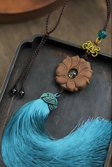 A wooden tray with a turquoise tassel and a brown flower-shaped pendant with a clear gem. 3