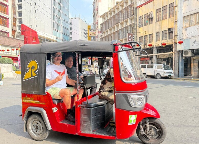 A red auto-rickshaw with two passengers and a dog, parked on a city street. 1