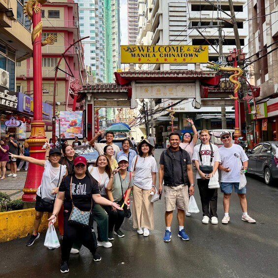 A group of people posing in front of a sign welcoming visitors to Manila Chinatown, with traditional Chinese architectural elements and a busy street scene. 4