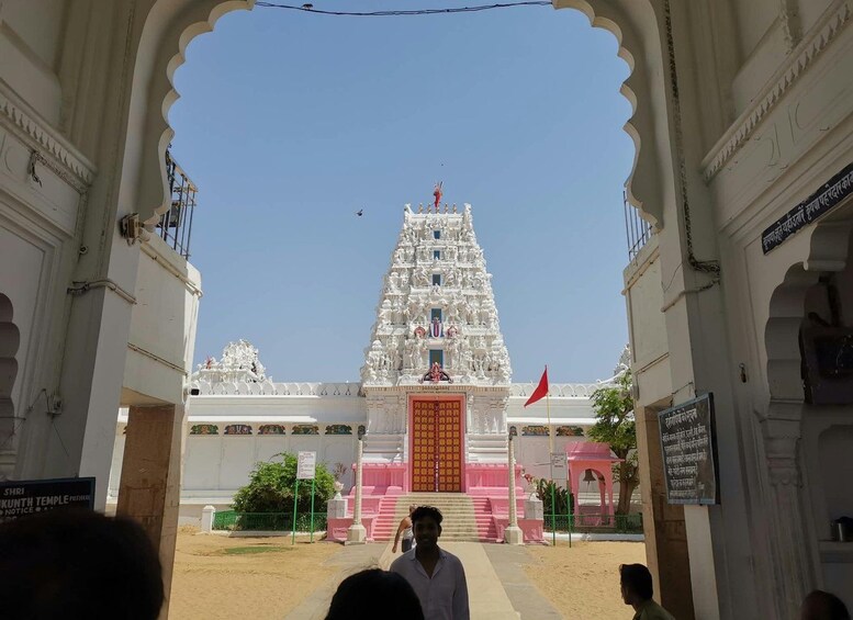 A white temple with a pink entrance, surrounded by white walls and a clear sky. 5