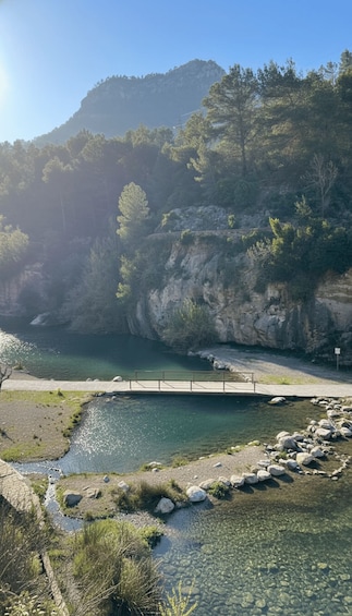 A clear river with a bridge, rocky terrain, and a forested hillside. 2