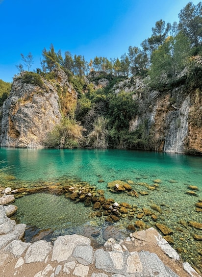 A clear turquoise lake surrounded by rocky cliffs and dense greenery. 1