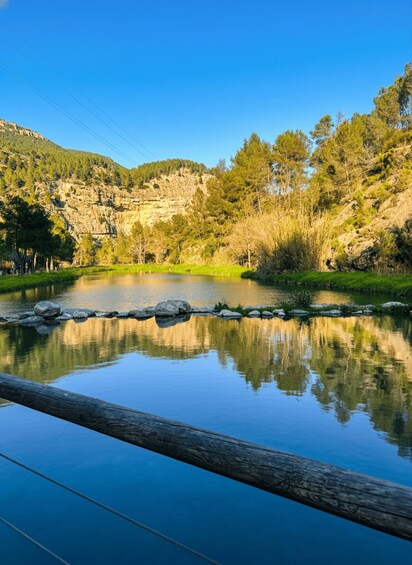 A calm lake with a wooden bridge in the foreground, surrounded by lush greenery and rocky cliffs. 5