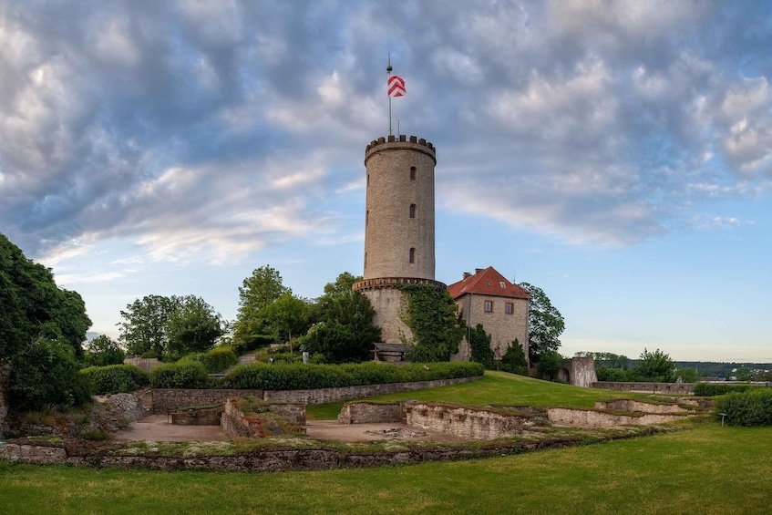 A historic tower with a flag, surrounded by lush greenery and a well-maintained lawn. 1