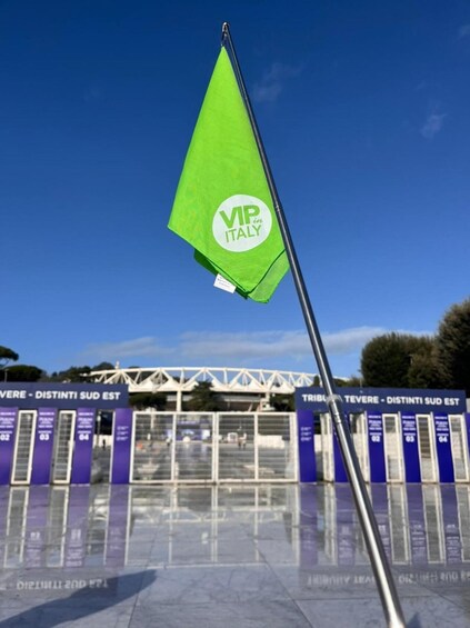 A green flag with 'VIP in ITALY' on a pole in front of a building with blue and white signage. 2