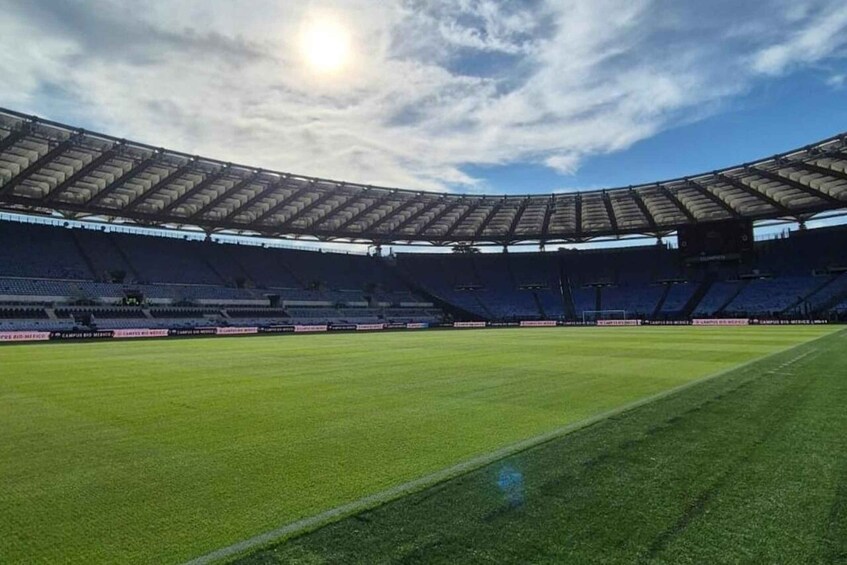A large, empty stadium with a green field and a partially covered roof. 1