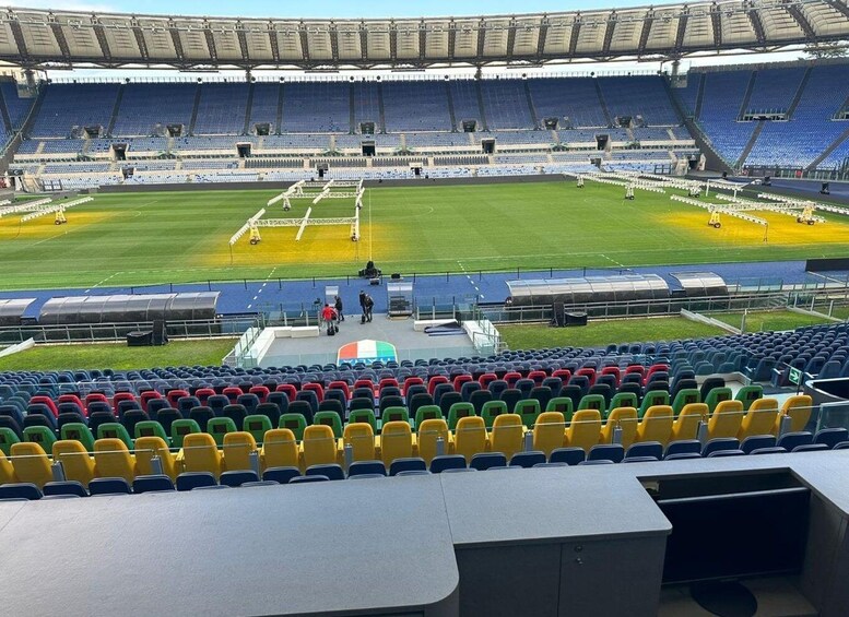A stadium with empty blue seats, a green field, and a stage with people. 5