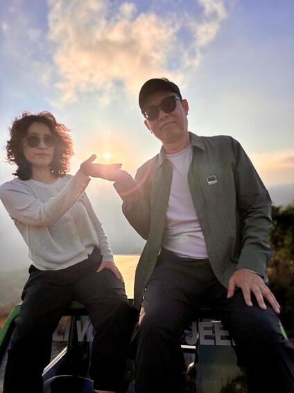 Two people sitting on a vehicle with a sunset in the background. 2