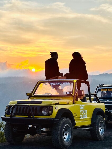 A yellow jeep with 'Bali Volcano Jeep' and 'Get Your Guide' text, two people sitting on the roof, and a sunset in the background. 3