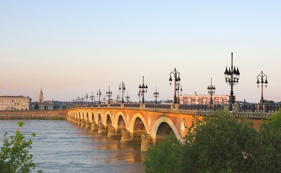 A stone bridge with multiple arches over a river, accompanied by street lamps and buildings in the background. 4