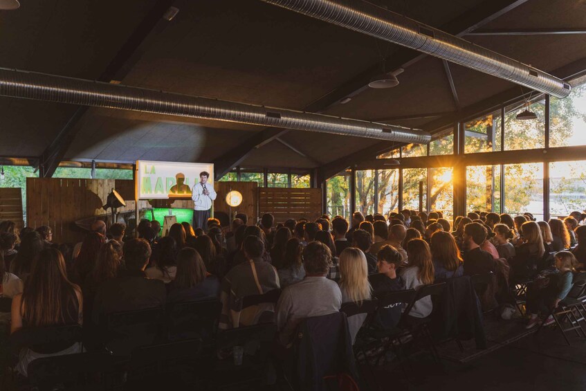 An indoor gathering with people seated facing a stage where a speaker is presenting. 2