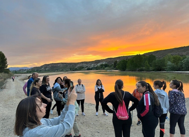 A group of people standing by a river during sunset. 2
