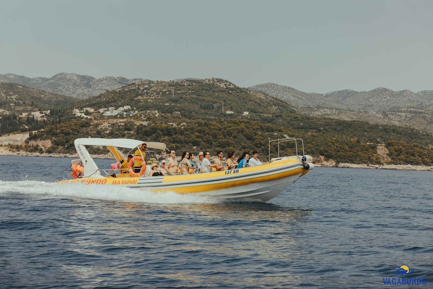 A yellow boat with passengers on a body of water, surrounded by hills and a coastline. 1