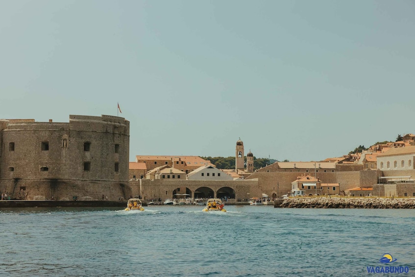A historic waterfront with a large stone fortress, a bell tower, and gondolas on the water. 2