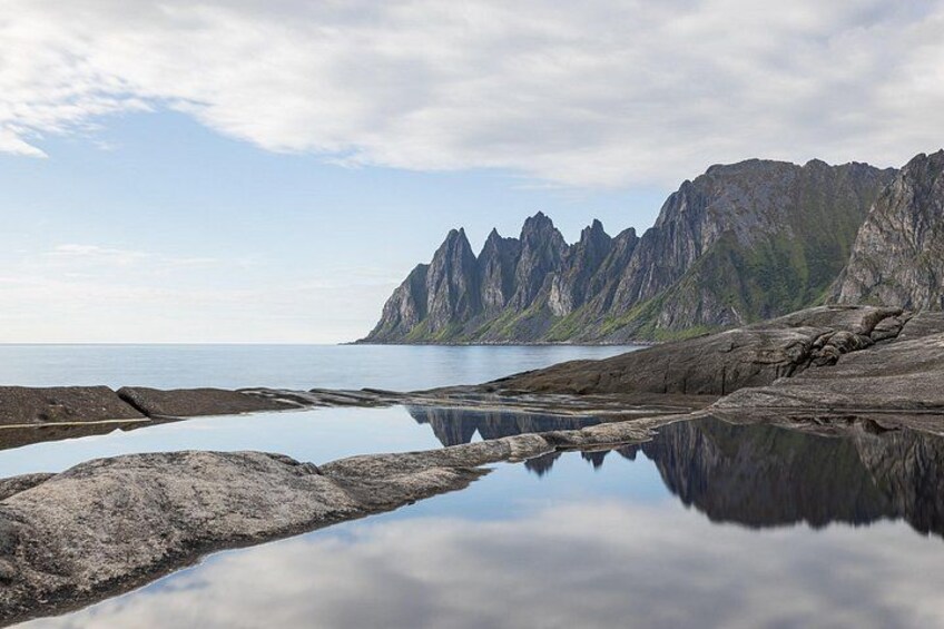 A coastal landscape with a calm sea, rocky shore, and a mountain range. 5